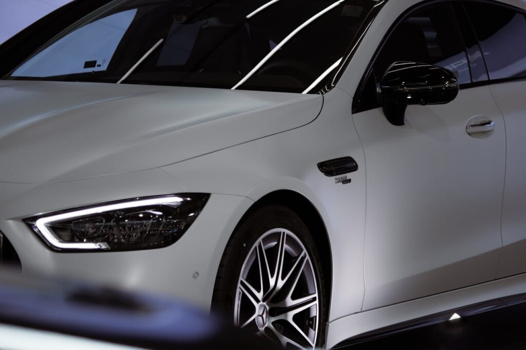 Close-up shot of a luxury white Mercedes Benz car in a showroom showcasing the sleek front design.